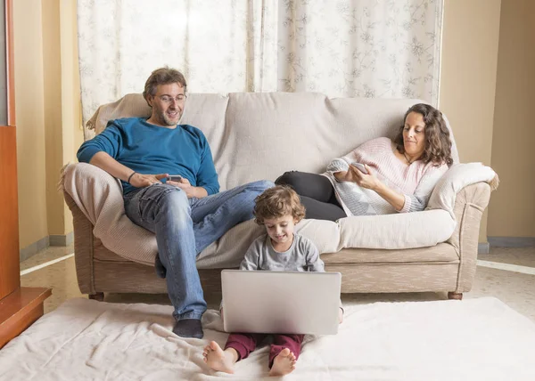 Çocuk, bir kadın ve bir erkek kanepede oturup dizüstü bilgisayar ve akıllı bir telefon izliyor..