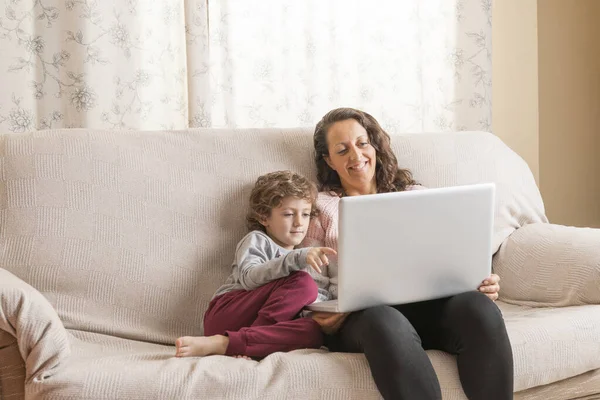 Çocuk ve kadın kanepede oturup dizüstü bilgisayar izliyorlar..