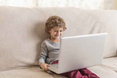Çocuk kanepede oturup dizüstü bilgisayar izliyor..