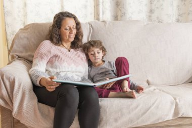 Çocuk ve bir kadın kanepede oturmuş kitap okuyorlar..