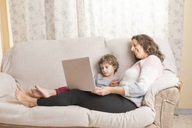 Çocuk ve kadın kanepede oturup dizüstü bilgisayar izliyorlar..