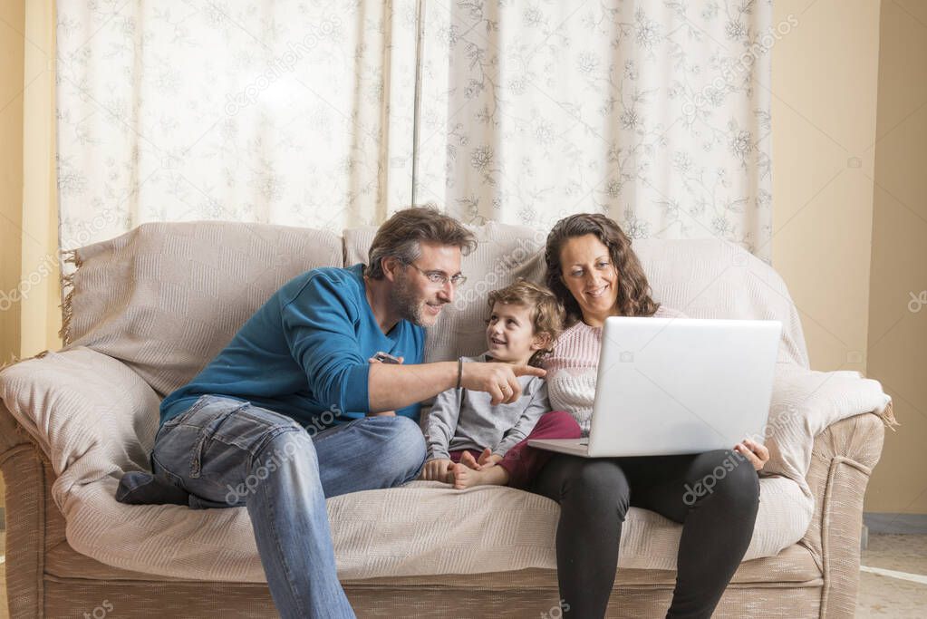 Child, a woman and a man sitting on a sofa watching a laptop and a smart phone.