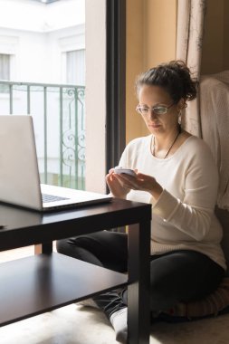 Bir kadın pencerenin önünde dizüstü bilgisayarın önünde oturuyor, evden işe gidip geliyor..