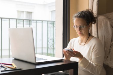 Bir kadın pencerenin önünde dizüstü bilgisayarın önünde oturuyor, evden işe gidip geliyor..