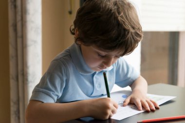 Pencerenin yanında ödev yapan çocuk,