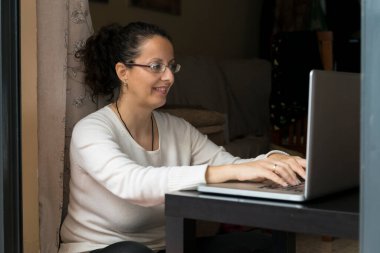 Bir kadın pencerenin önünde dizüstü bilgisayarın önünde oturuyor, evden işe gidip geliyor..