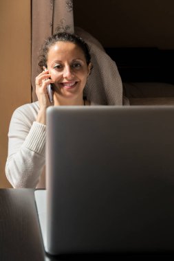 Bilgisayarın önünde akıllı telefondan konuşan bir kadın. Telekom konsepti.