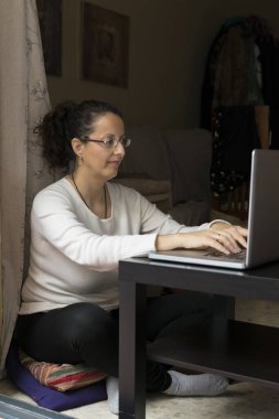 Bir kadın pencerenin önünde dizüstü bilgisayarın önünde oturuyor, evden işe gidip geliyor..