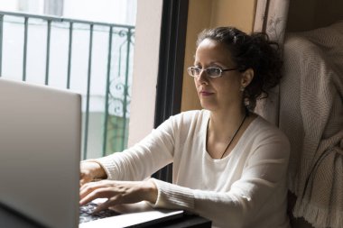 Bir kadın pencerenin önünde dizüstü bilgisayarın önünde oturuyor, evden işe gidip geliyor..