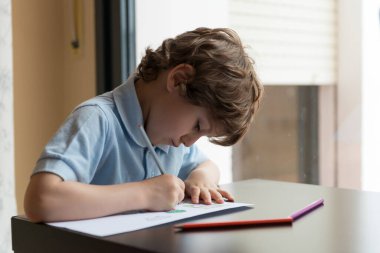 Pencerenin yanında ödev yapan çocuk,