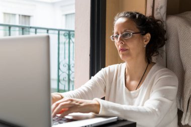 Bir kadın pencerenin önünde dizüstü bilgisayarın önünde oturuyor, evden işe gidip geliyor..