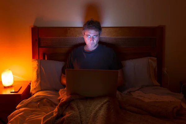 A man sitting on the bed watching the laptop. Telework concept.