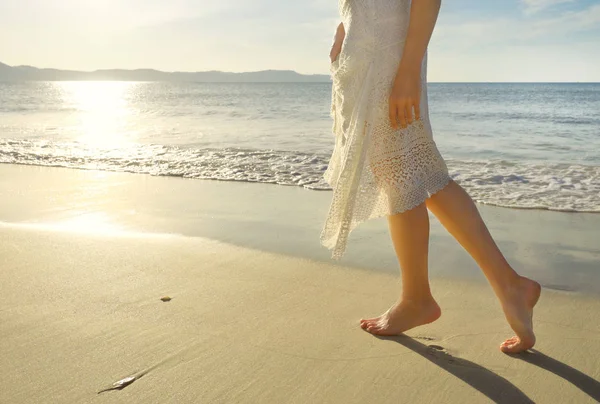 Молодая женщина в белом платье ходит одна по песчаному тропическому пляжу — стоковое фото