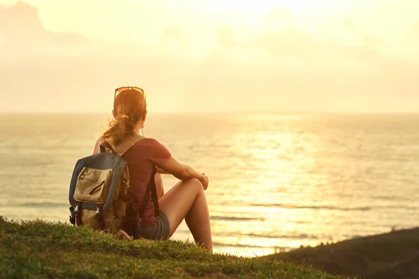 Молодая девушка с рюкзаком наслаждается закатом, слушая музыку на p — стоковое фото