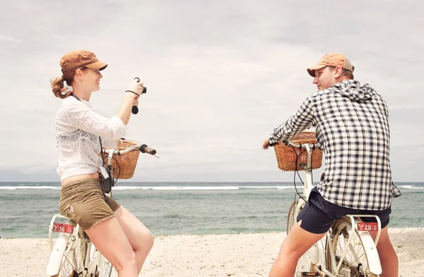 Casal alegre está tendo descanso e tirar fotos na praia com bicicletas à moda antiga . — Fotografia de Stock