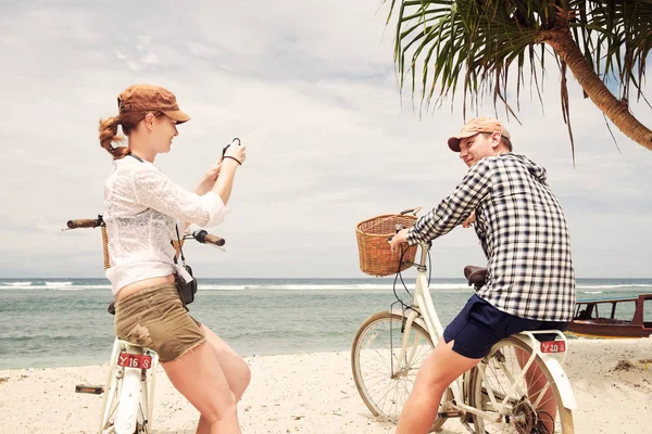 Fröhliche Frau fotografiert ihren Freund an der Küste mit einem altmodischen Fahrrad. — Stockfoto