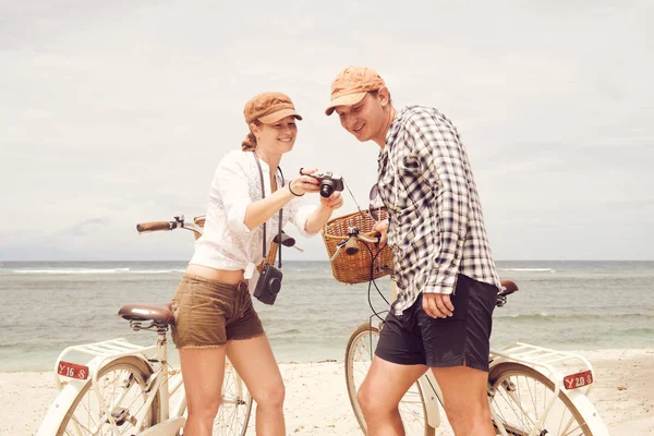 Lyckliga par med gamla gammaldags cyklar ser ut på bilderna på stranden. — Stockfoto