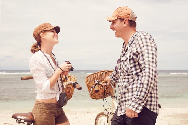 Jóvenes alegres hablando y sonriendo mientras están de pie cerca de sus bicicletas anticuadas en la playa . — Foto de Stock