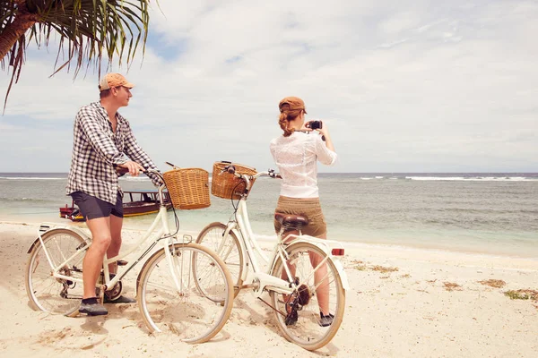 Gelukkige paar fotograferen kijkt naar zee permanent in de buurt van hun ouderwetse fietsen op theon strand. — Stockfoto