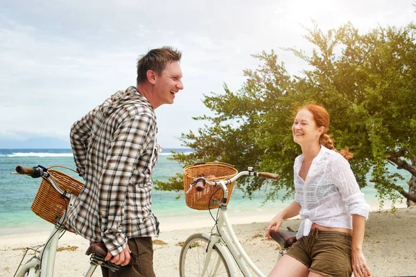 Jovens alegres conversando e sorrindo enquanto estão perto de suas bicicletas à moda antiga na praia . — Fotografia de Stock