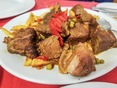 Kızarmış patatesli yahni ve porselen tabakta servis edilen yeşil bezelye.