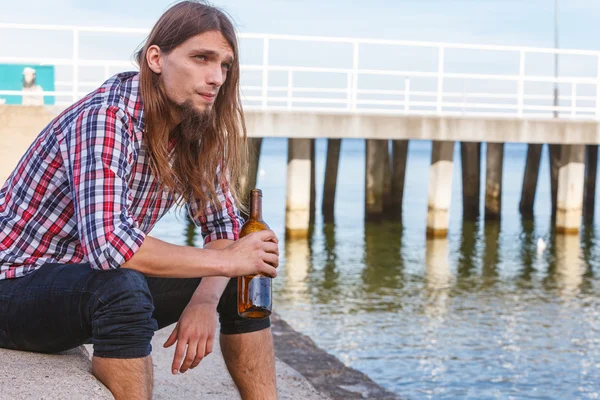 Man depressed with wine bottle sitting on beach outdoor — Stock Photo, Image