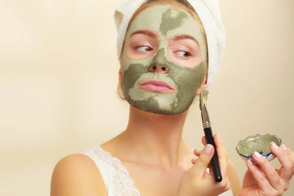 Woman applying with brush clay mud mask to her face