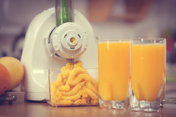 Making orange juice in juicer machine in kitchen — Stock Photo, Image