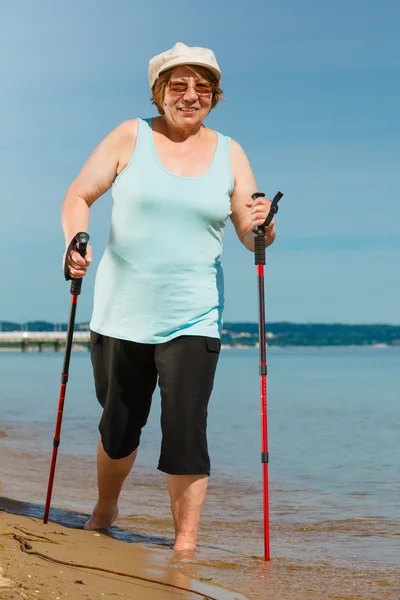 Starší žena cvičí na nordic walking na pláži — Stock fotografie