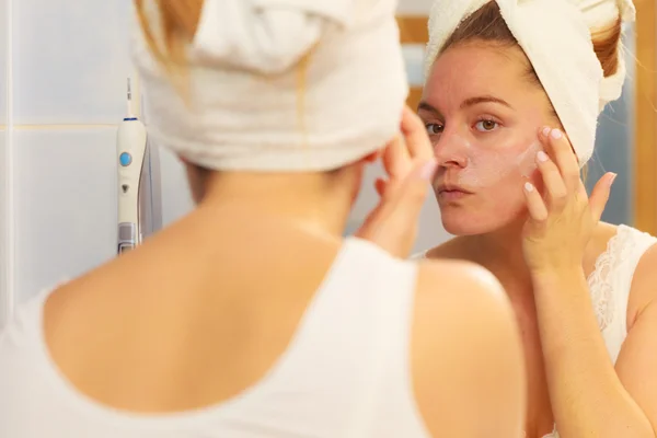 Mulher aplicando creme máscara no rosto no banheiro — Fotografia de Stock