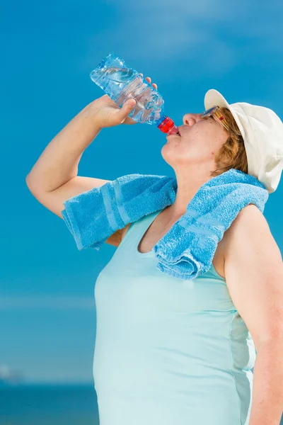 Old woman drinking mineral water in plastic bottle outdoor — Stock Photo, Image