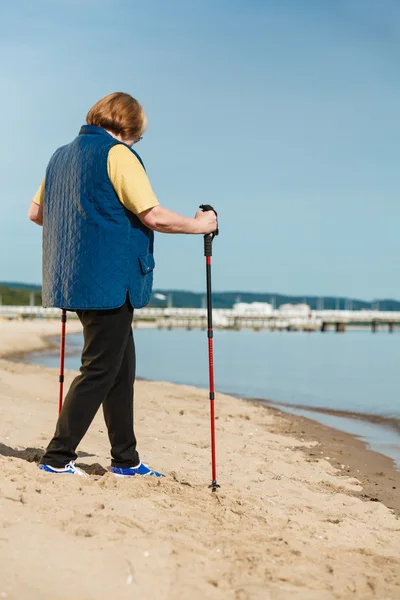 Senior woman practicing nordic walking on beach — Stock Photo, Image