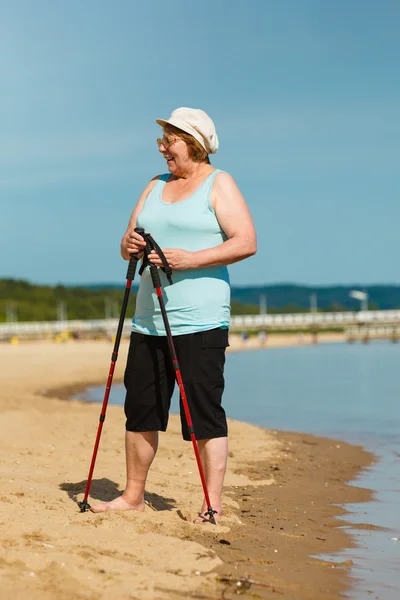 Senior Kvinna tränar stavgång på stranden — Stockfoto