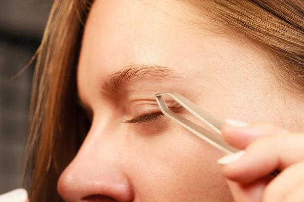 Woman tweezing eyebrows depilating with tweezers