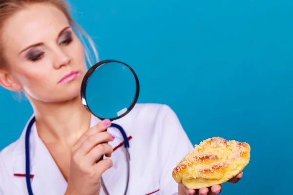 Doctor with magnifying glass examining sweet food — Stock Photo, Image