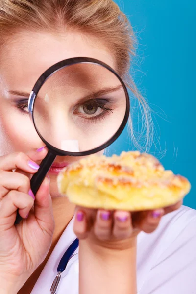 Doctor with magnifying glass examining sweet food — Stock Photo, Image