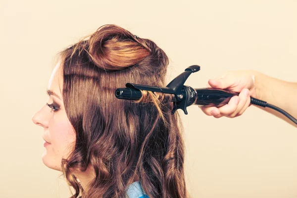 Stylist krullend haar voor jonge vrouw. — Stockfoto