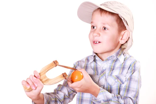 Junge schießt mit Schleuder auf Mandarine. — Stockfoto