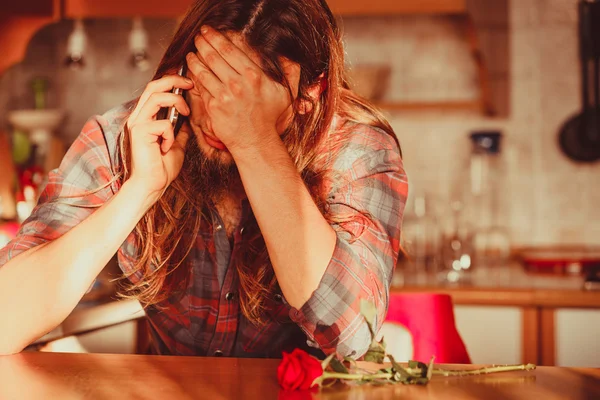 Worried man with rose and mobile phone.