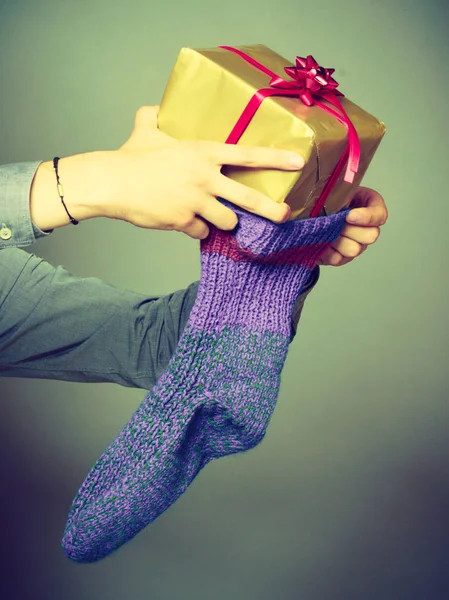 Male hands putting wrapped gift in knitted christmas sock — Stock Photo, Image