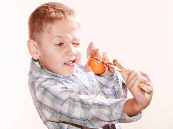 Junge schießt mit Schleuder auf Mandarine. — Stockfoto