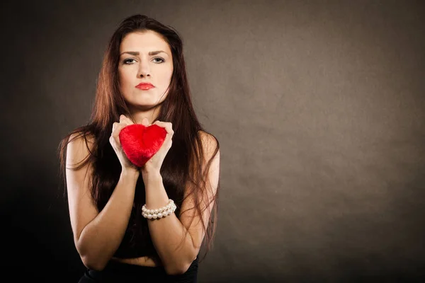 Triste mujer encantadora sostiene el corazón rojo en negro — Foto de Stock