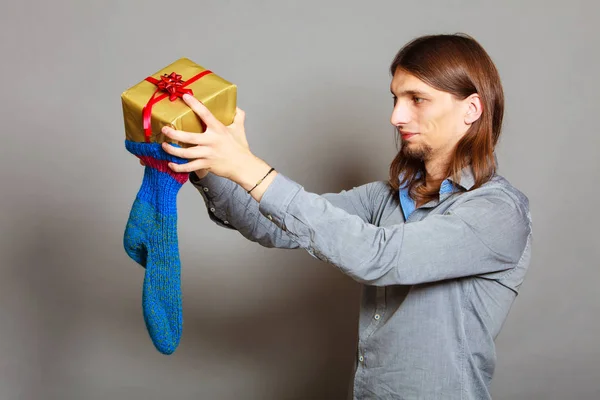 Хлопець кладе загорнутий подарунок у в'язану різдвяну шкарпетку — стокове фото
