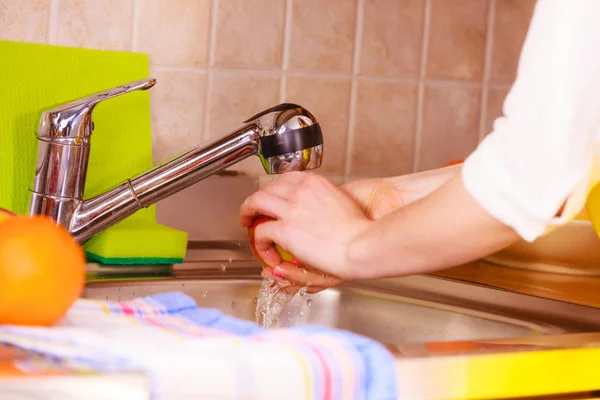 Huisvrouw wassen van fruit in de keuken onder water stroom — Stockfoto