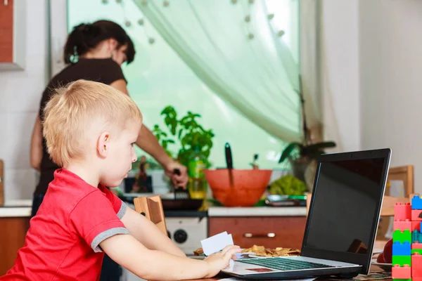 Bambino con laptop e mamma che cucina in cucina . — Foto Stock