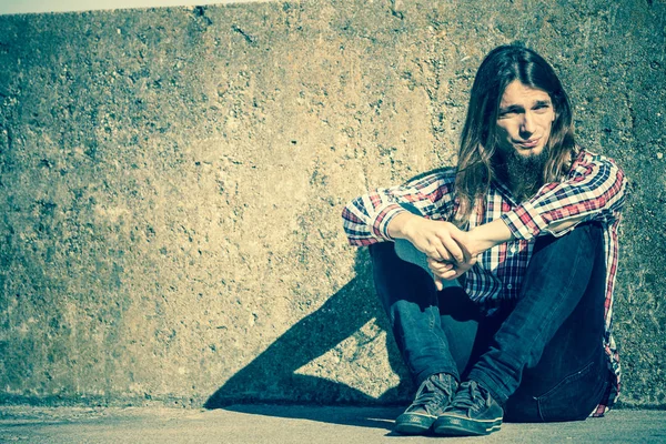 Hombre de pelo largo sentado solo triste en la pared grunge — Foto de Stock