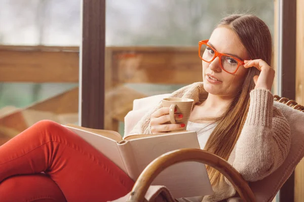 Mujer sentada en silla leyendo libro en casa —  Fotos de Stock