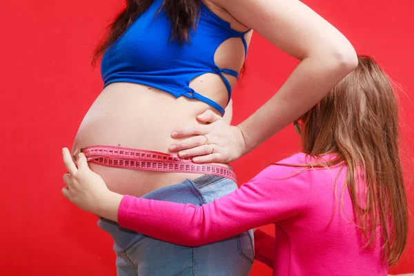 Filha medindo barriga de mulher grávida com fita — Fotografia de Stock