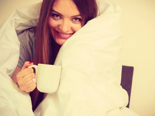 Mujer sonriente sosteniendo una taza de bebida en la cama —  Fotos de Stock