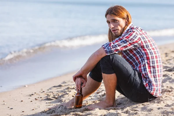 ชายที่หดหู่กับขวดไวน์ นั่งอยู่บนชายหาดข้างนอก — ภาพถ่ายสต็อก